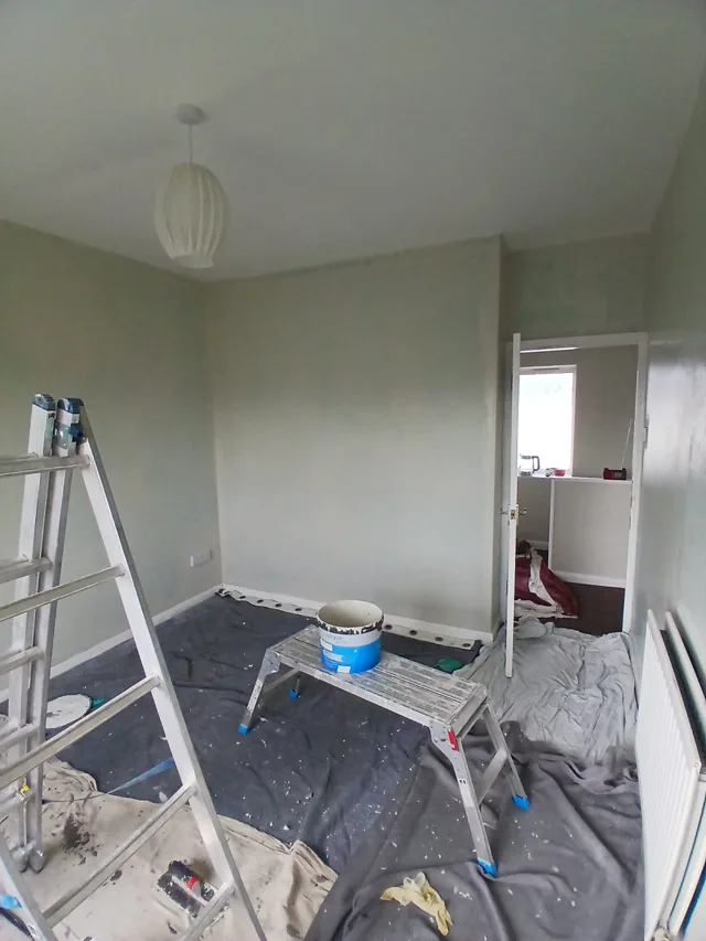Room decorating in progress with dust sheets and painting equipment.